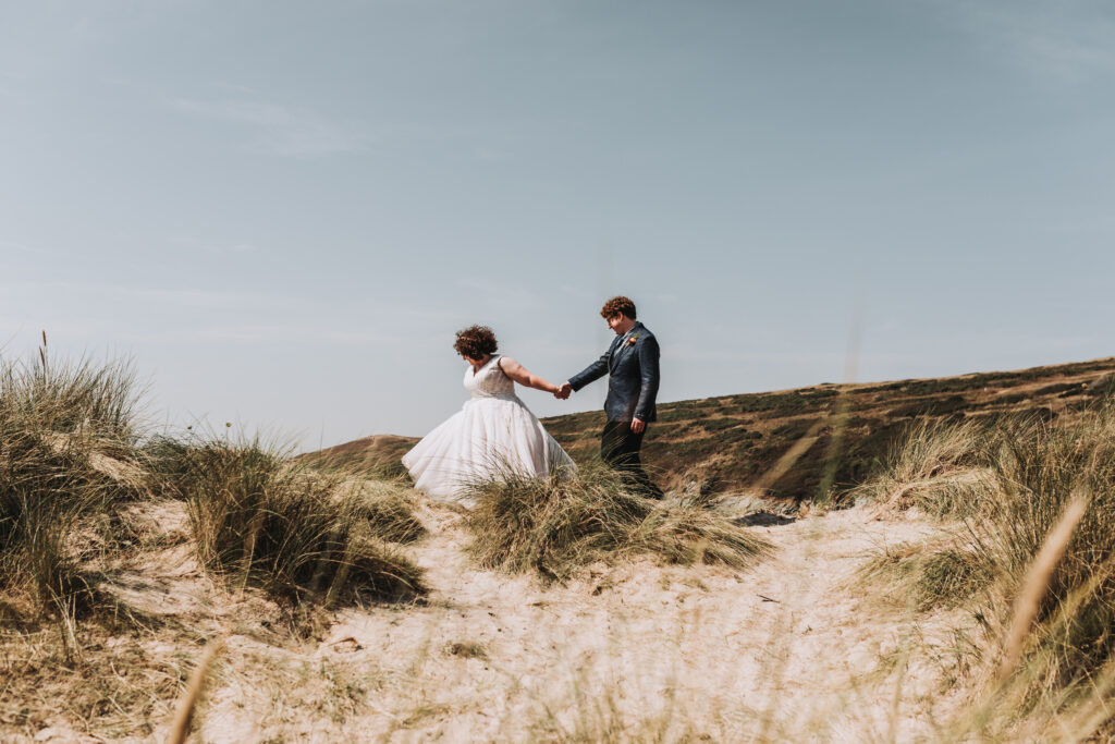 couple walking through dunes after getting married in cornwall