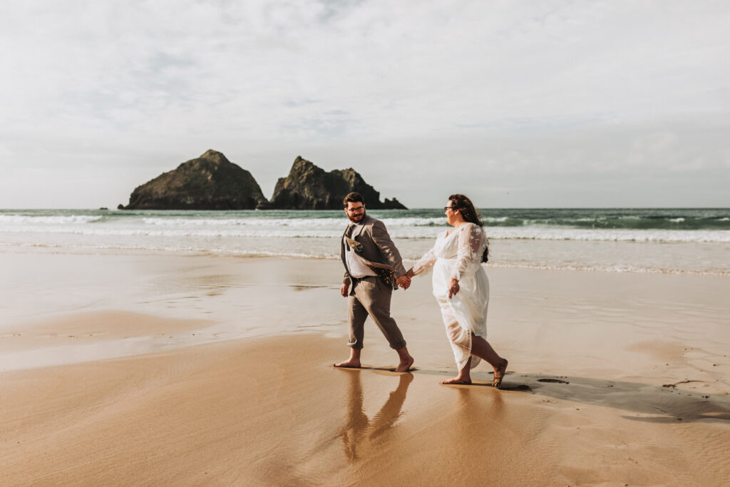 newlywed couple walking on cornish beach