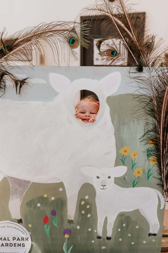 little girl poking her head through wooden cut out of sheep