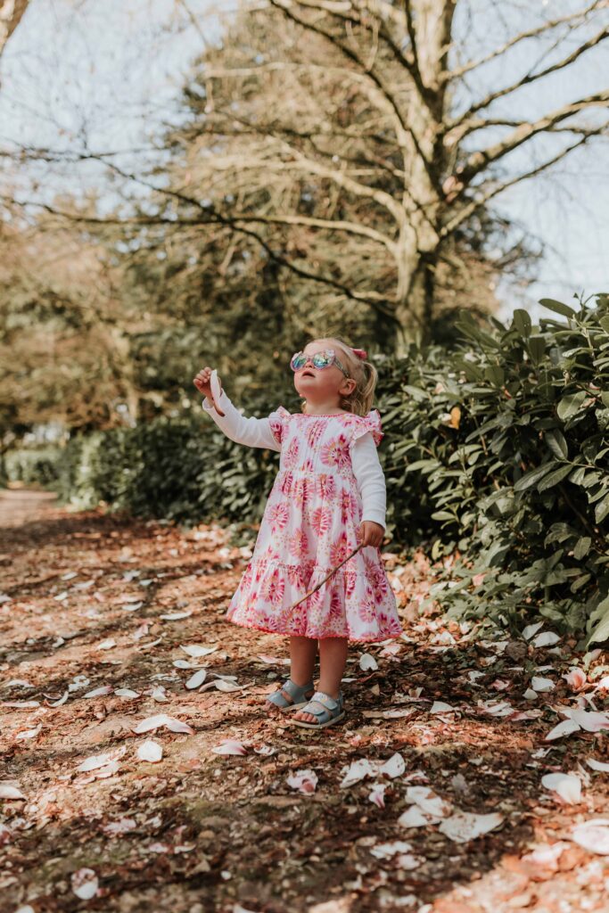 little girl in pink dress with sunglasses looking up to the sky holding a stick