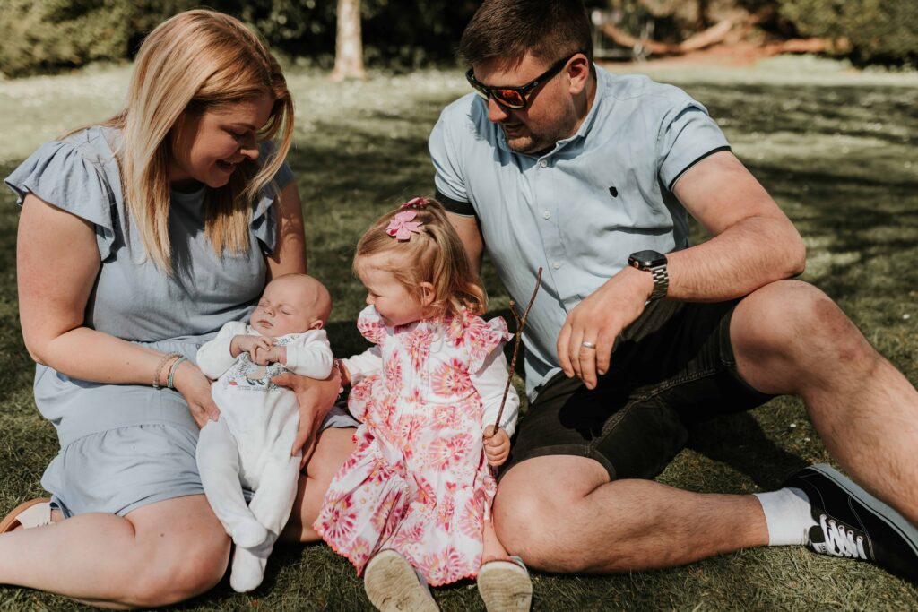 family of four mum dad and one daughter and one son sat around on the grass together