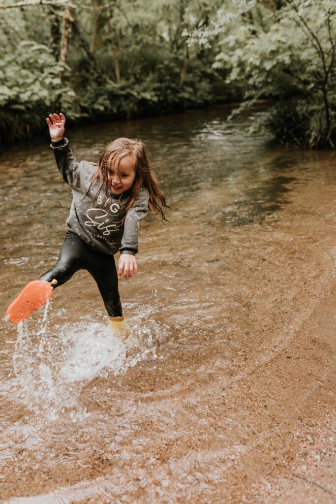 little girl splashing in a river with wellies on at family photoshoot in cornwall