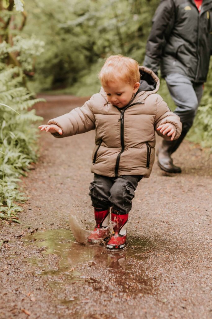 little boy jumping into a puddle at family photoshoot in cornwall