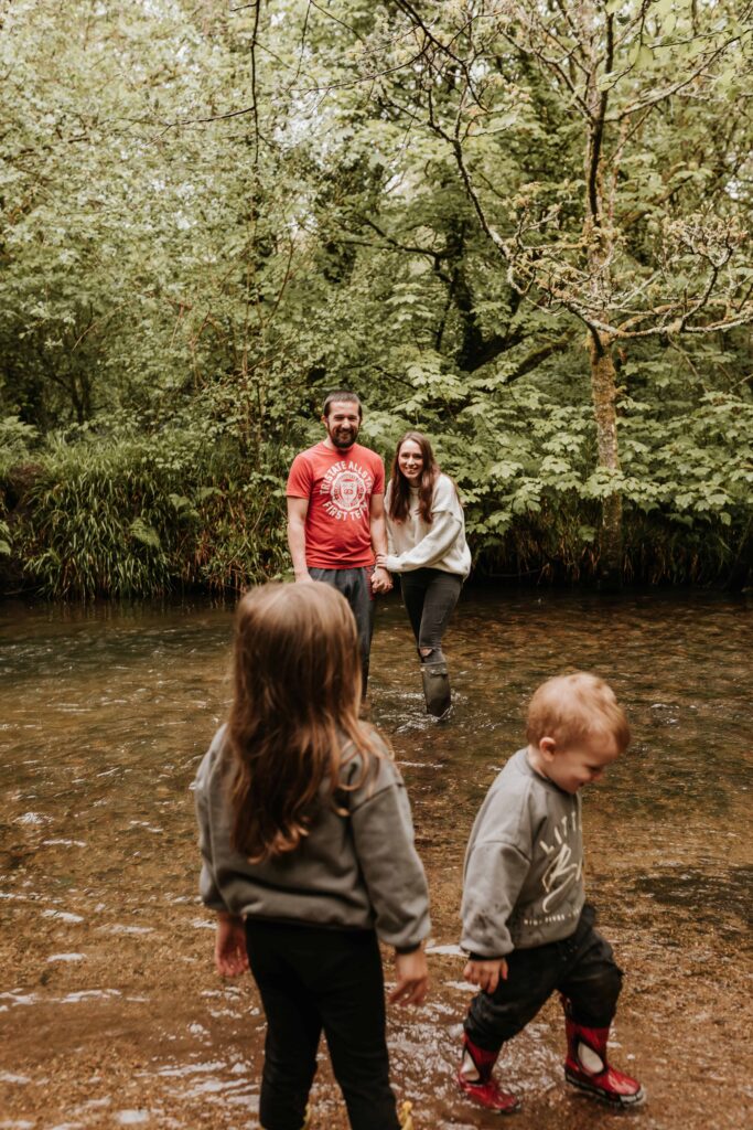 mum and dad standing together in river whilst kids look from the river bank