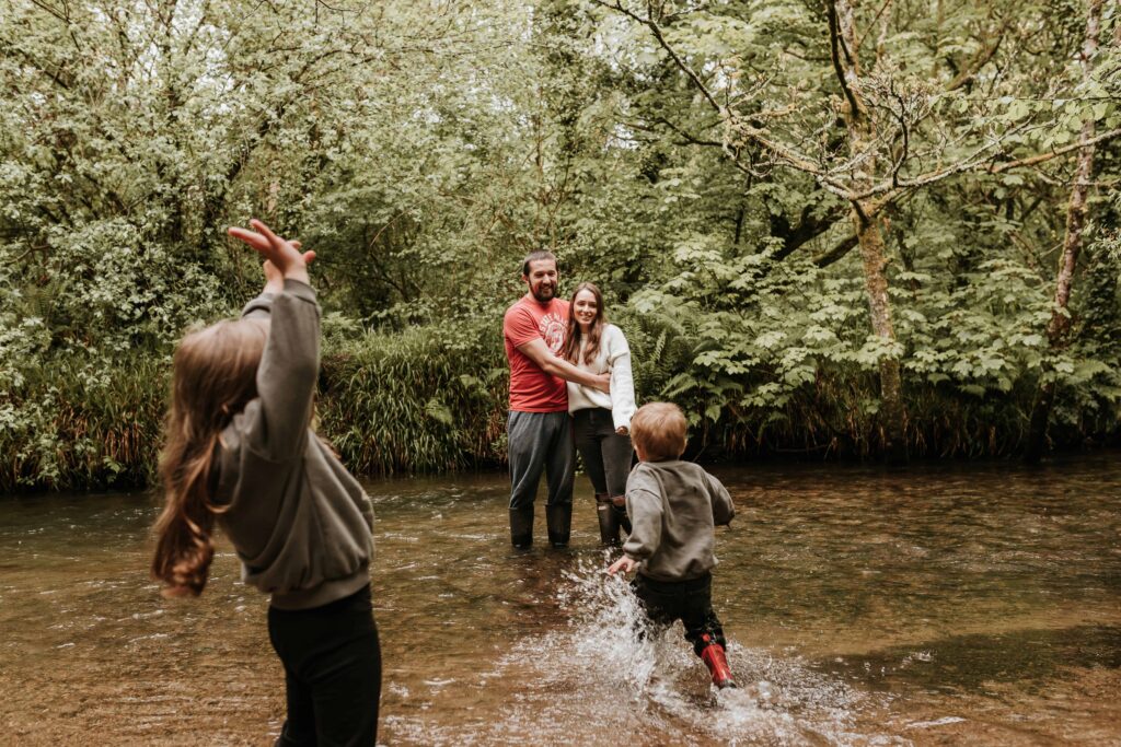mum and dad standing together in river whilst son runs towards them splashing