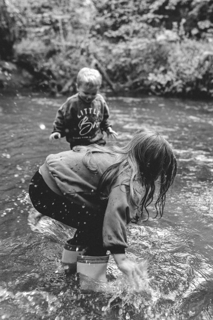 little girl and boy splashing in the river with their hands and feet at family photoshoot in cornwall