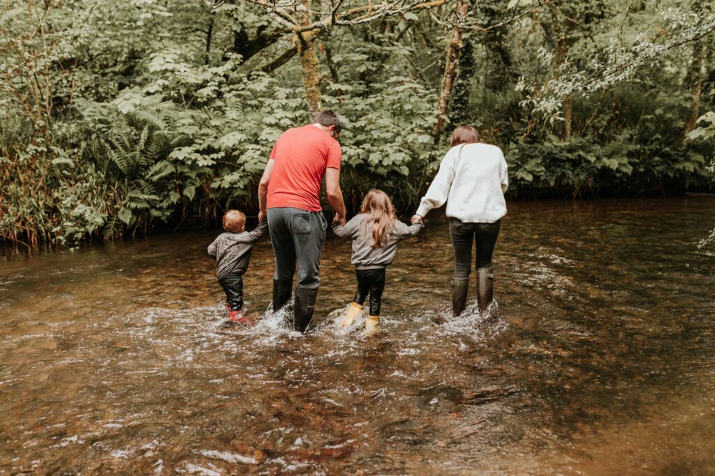 son dad daughter and mum walking up stream all in wellies at family photoshoot in cornwall