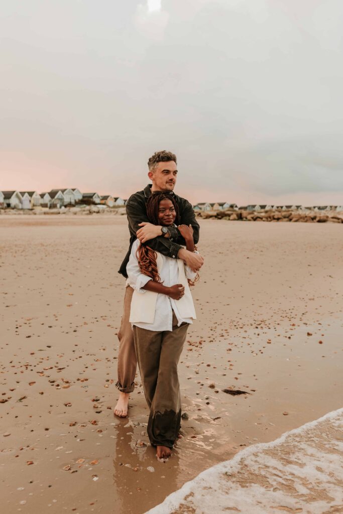 man cuddling woman from behind on a beach at mudeford