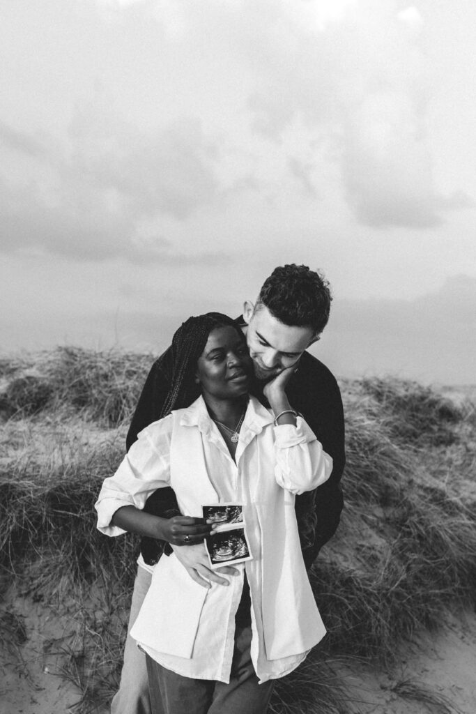 man and woman cuddling whilst she holds baby scan photo