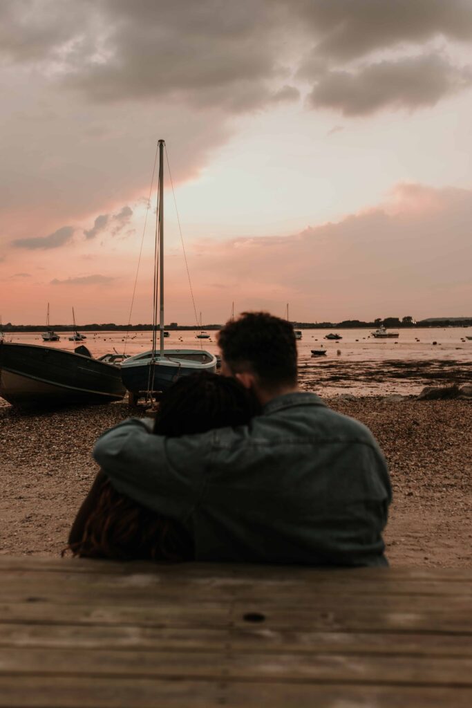 man and woman cuddling as the sun sets near moored boats