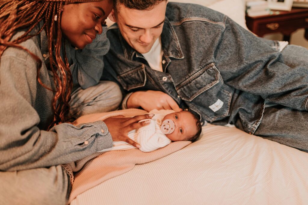 mum and dad lay on bed whilst looking at their newborn baby at maternity & newborn photoshoot