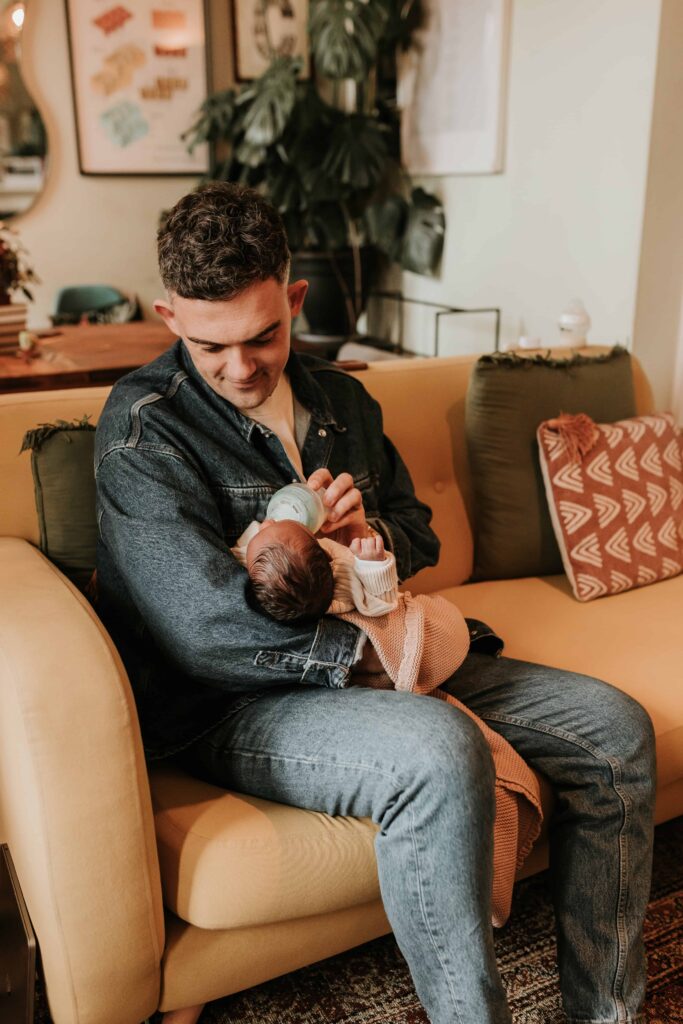 dad holds newborn baby whilst feeding her from a bottle