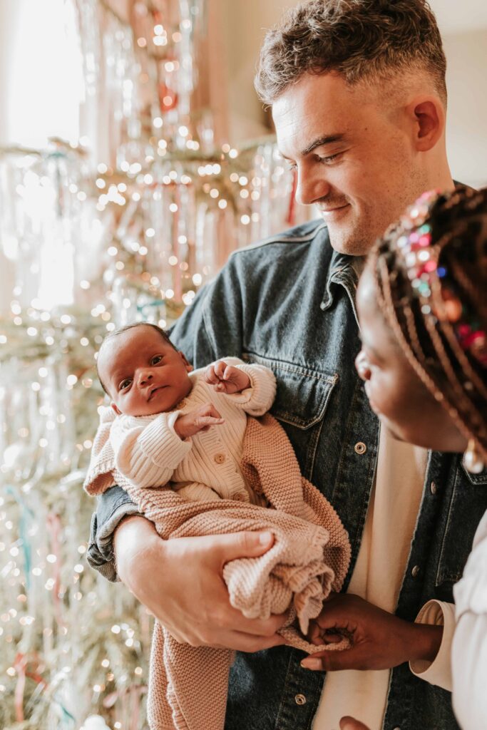dad holds newborn baby by christmas tree