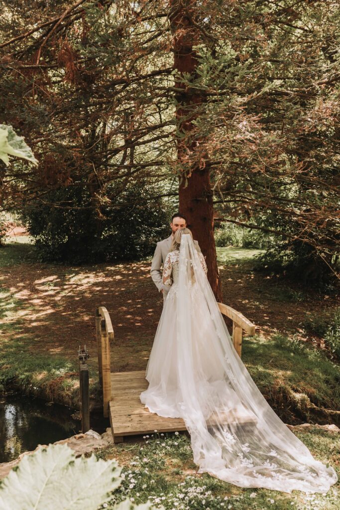 brides dress and veil as couple stand on a bridge
