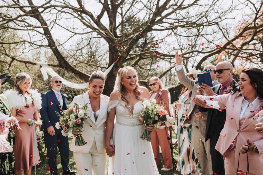 two brides smiling walking through confetti