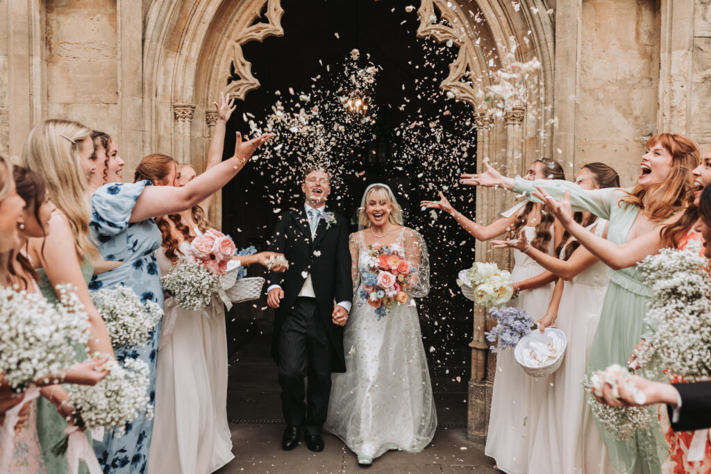 bride and groom walking out of church into confetti smiling
