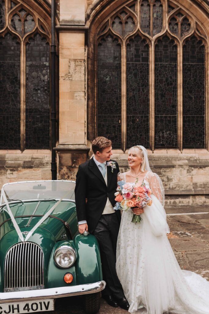 bride and groom looing at eachother leant against vintage car