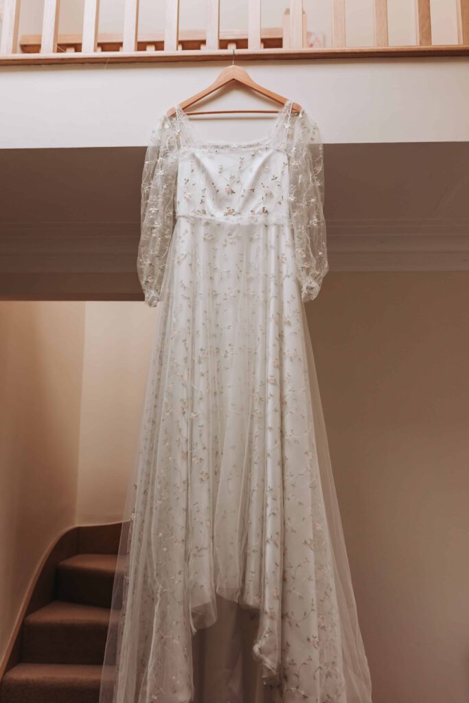 white wedding dress hanging from shelf with embroidered flowers on