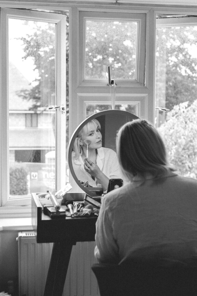 bride doing her own makeup in circle mirror