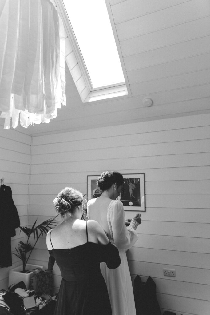 bride having her dress done up by friend