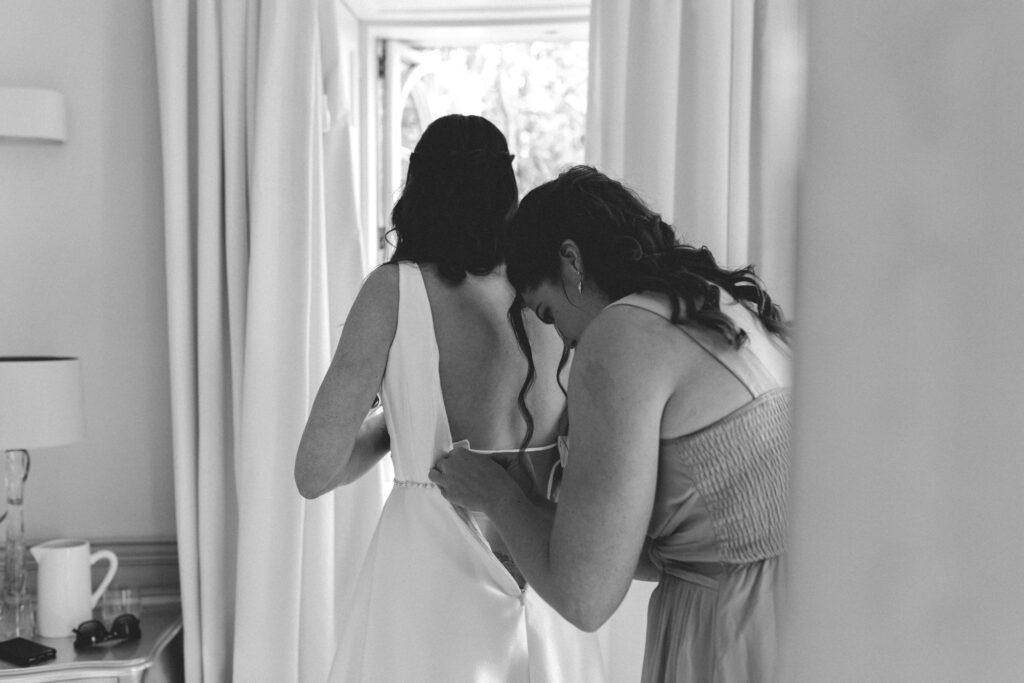 bridesmaid doing up brides dress
