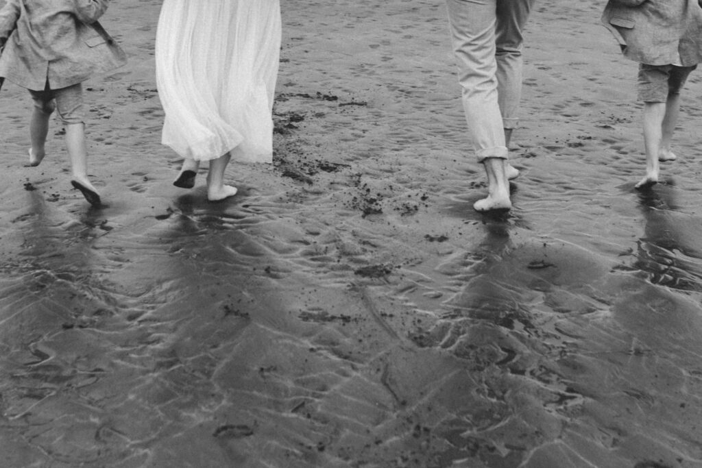 feet of family of four running along the beach