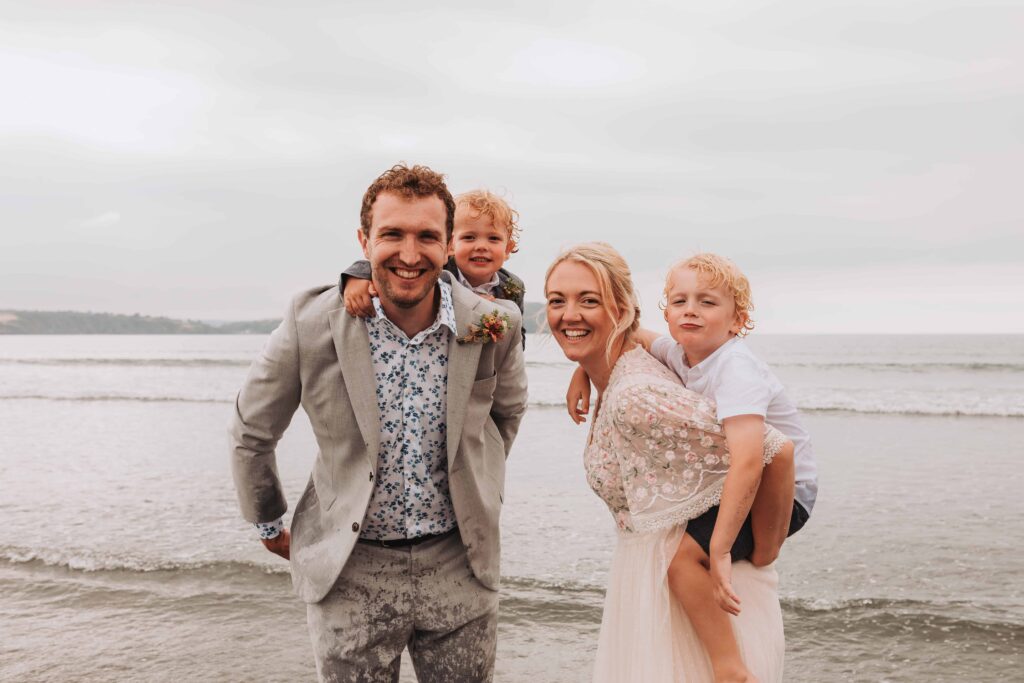 family of four with sons having piggy backs from mum and dad on wedding day