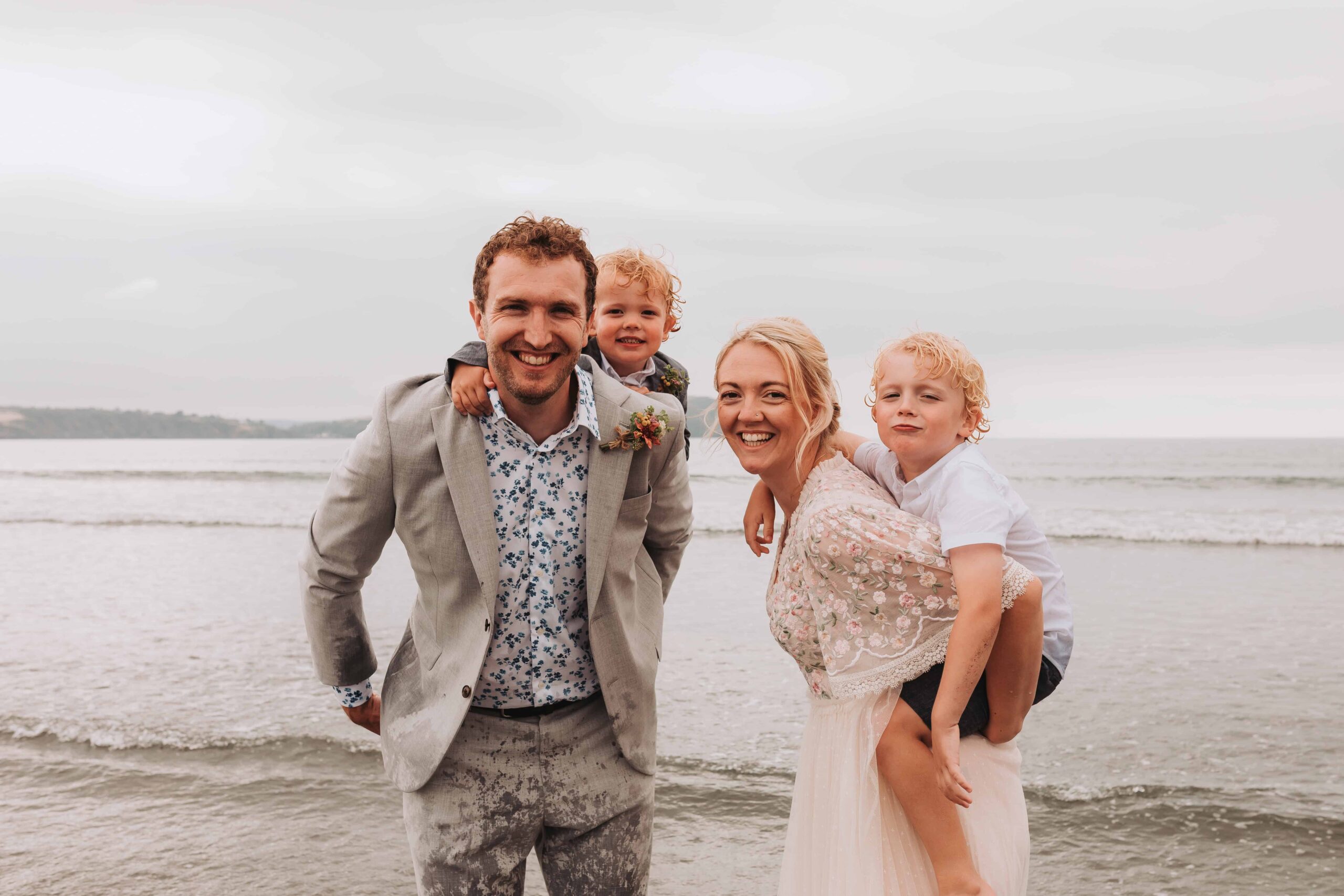 family of four with sons having piggy backs from mum and dad on wedding day