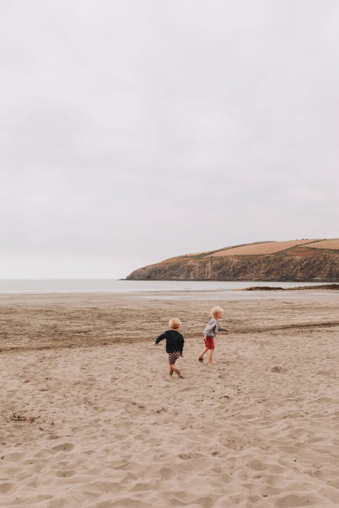 two young boys running around on a beach in pembrokshire