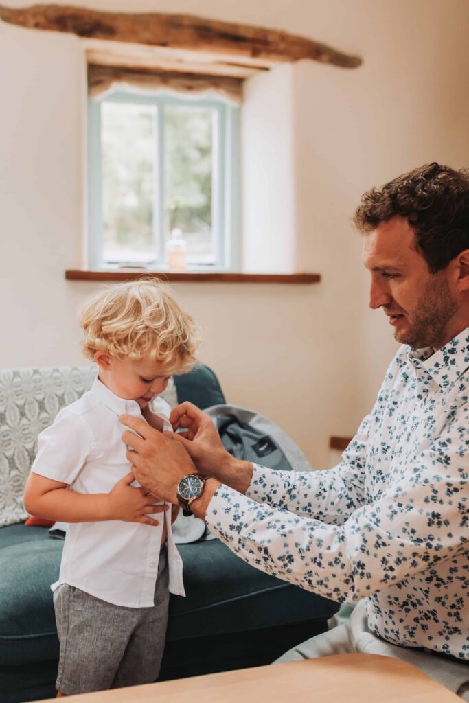 dad doing up young sons shirt on wedding day