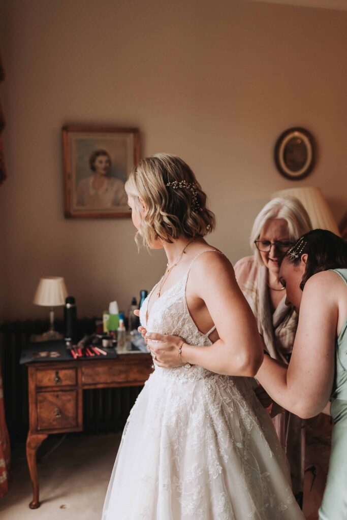 bride having her dress done up at wadhurst castle wedding
