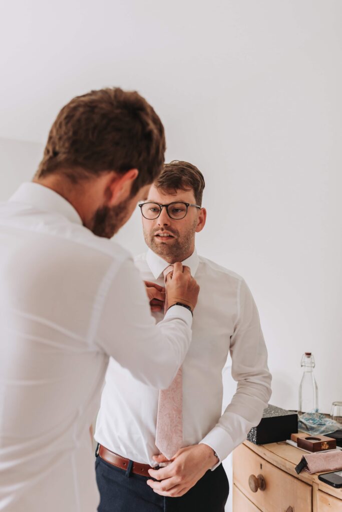 groom having his tie done up by best man