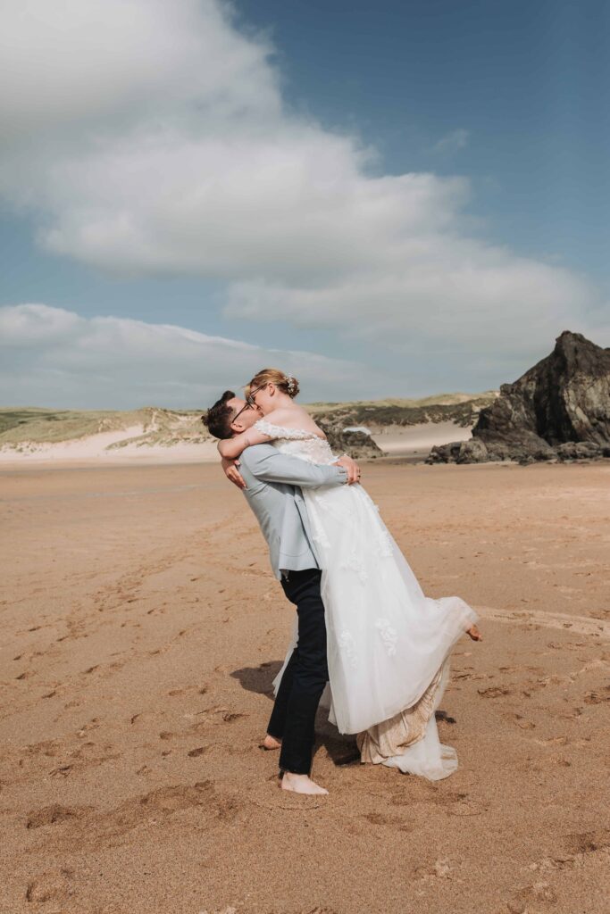 groom lifting bride up on holywell bay beach