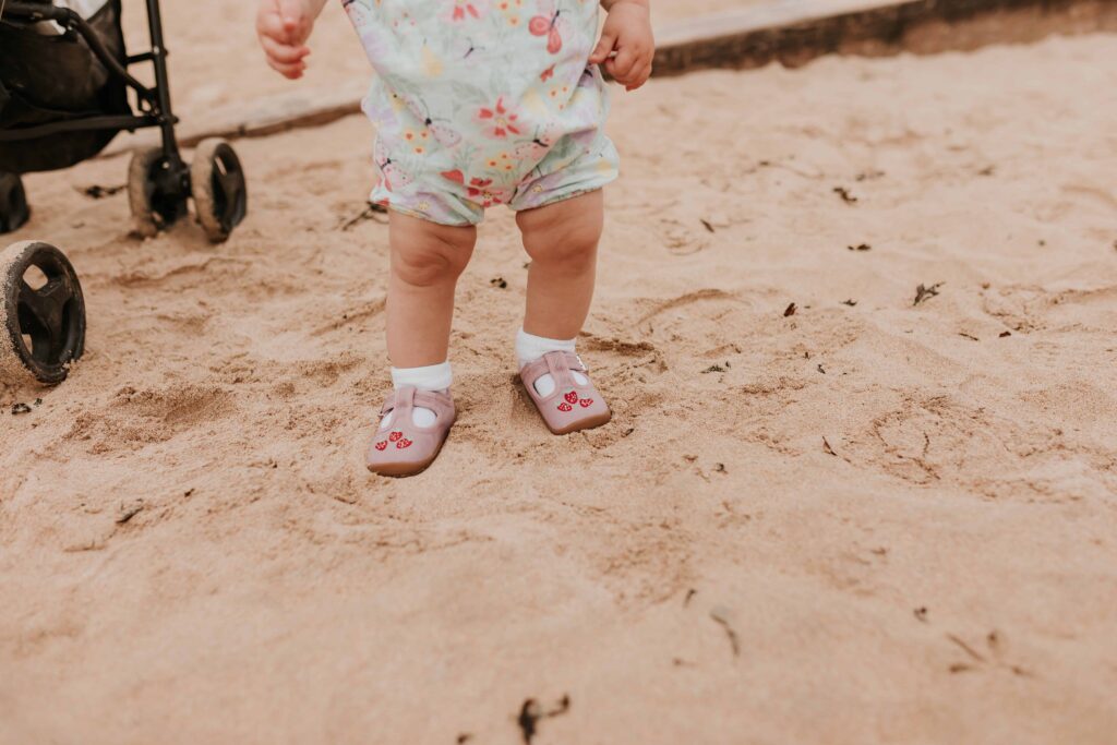 little girls legs and feet wearing shoes with straberries on and she is on the beach