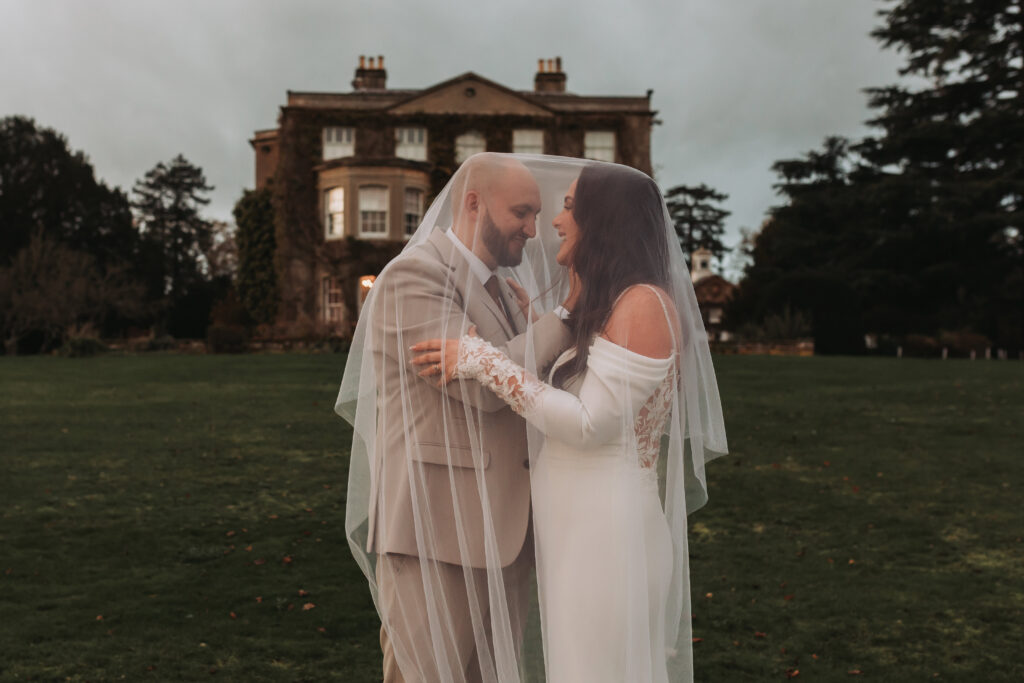 bride and groom smiling under brides veil in front of northbrook park