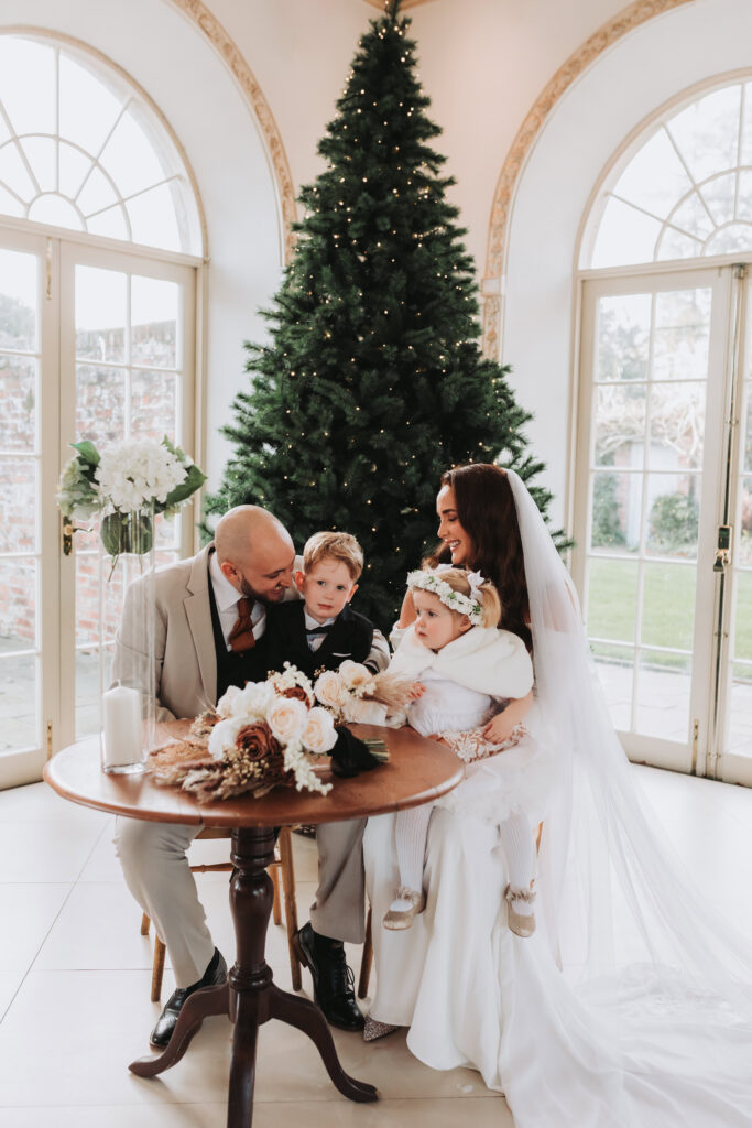 bride and groom signing the register with their two children in front of a christmas tree