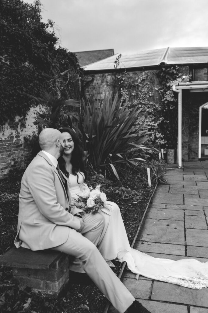 bride and groom sitting on a bench laughing at eachother