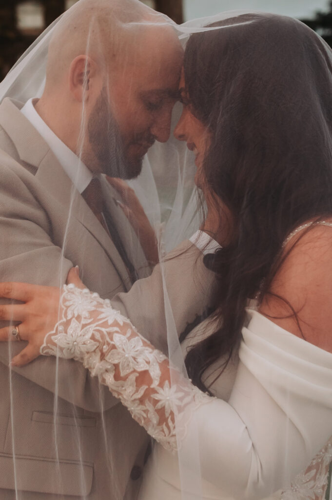 bride and groom touching foreheads underneath a veil