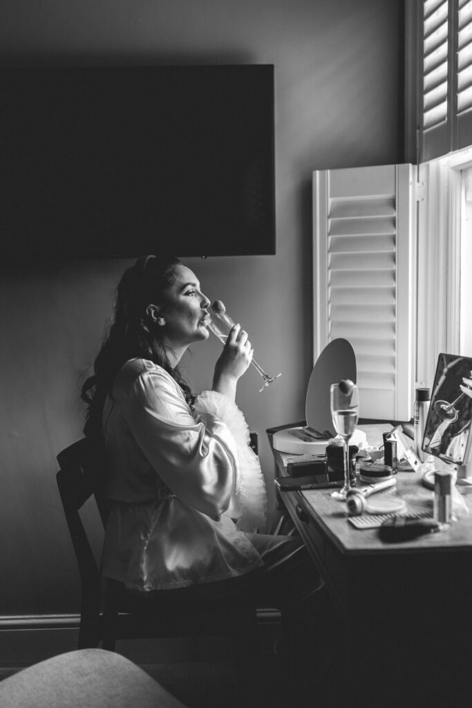 bride drinking glass of champagne getting ready at make up desk