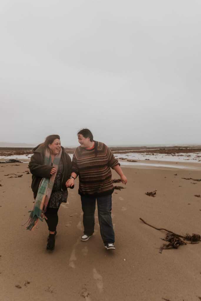 two girls laughing walking along marazion beach in the rain
