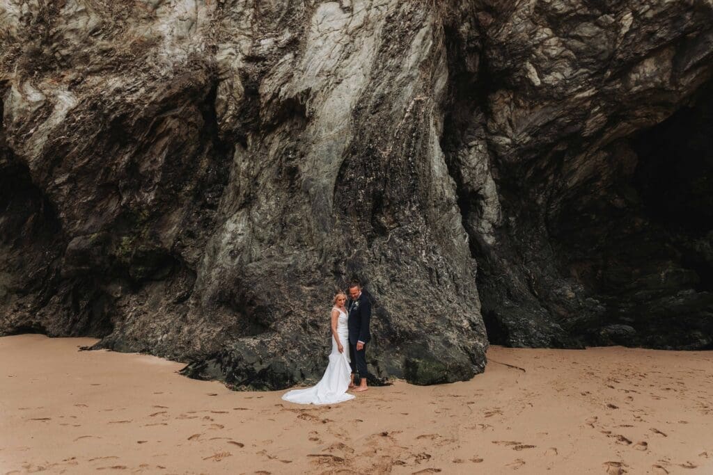 bride and groom stood in front of cliff face on a beach