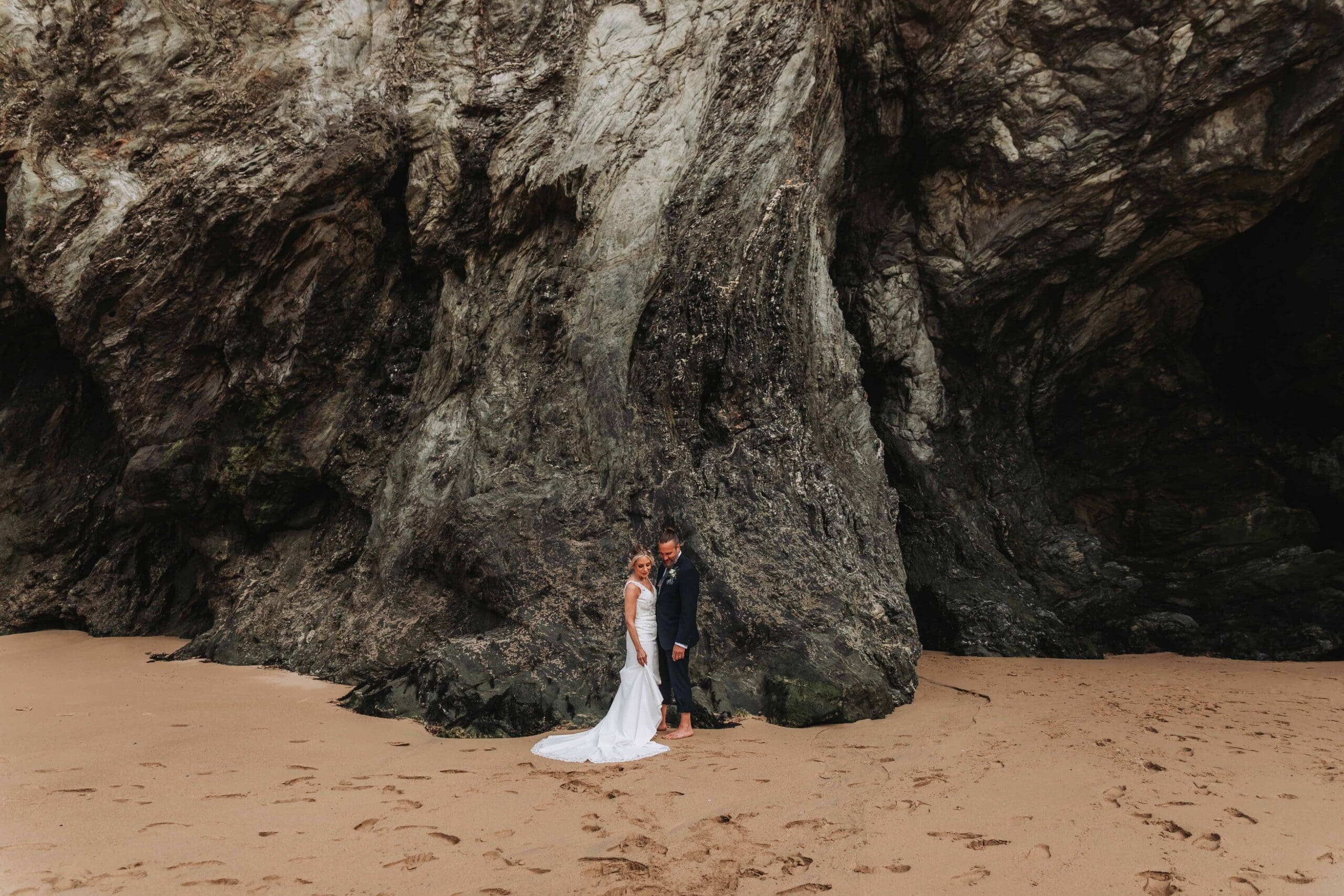 bride and groom stood in front of cliff face on a beach