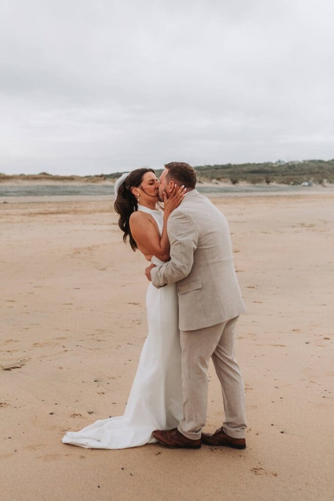 bride and groom kissing each other on cornish beach