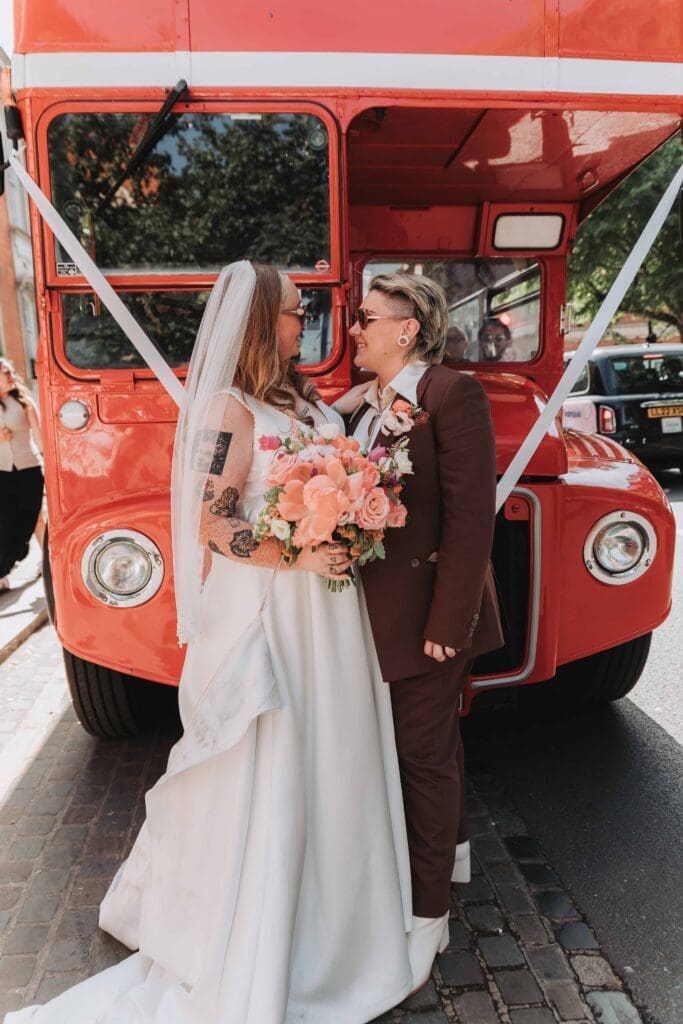 two brides holding each other in front of red double decker bus in london