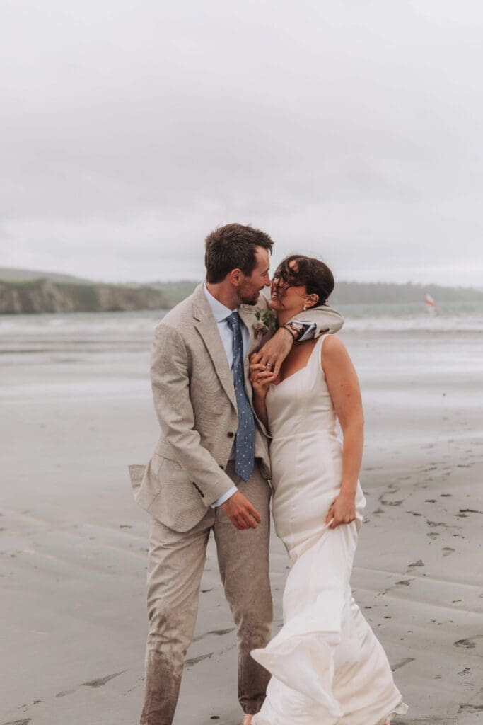 bride and groom holding each other on beach walking