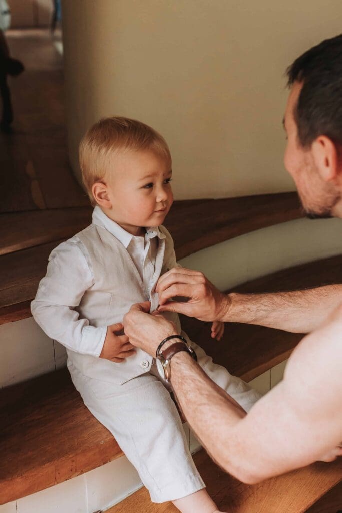 groom doing toddler sons waistcoat up after deciding to elope in the uk