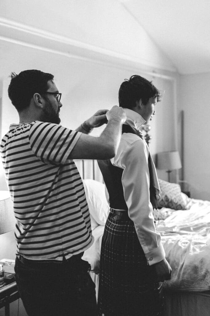 groom helping son get dressed at woodland wedding
