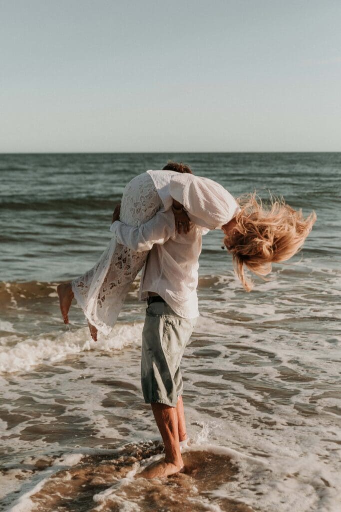 guy carrying girl over his shoulder at beach couple photoshoot