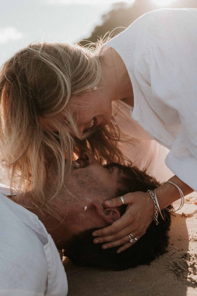 girl kissing guy on the beach when he is laid down