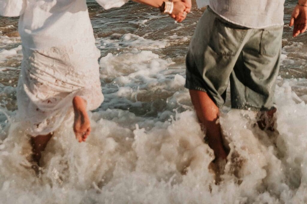 guy and girl plashing through the sea at beach couple photoshoot
